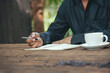 © aFotostock - Man hands writing notebook diary with coffee cup and smartphone on wood desk. Close up man hands using pen sitting at wooden table outdoors lifestyle. Men write planner note diary office agenda