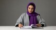 © Cuan - A woman in a hijab thoughtfully writes in a notebook, showcasing elegance and focus.