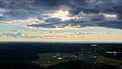 Wall Mural - Dark stormy clouds with sun rays shining through above Latvia landscape, aerial view