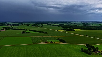 Wall Mural - Stormy clouds over rural farmland with distant houses, fields, and rolling hills in moody dark lighting