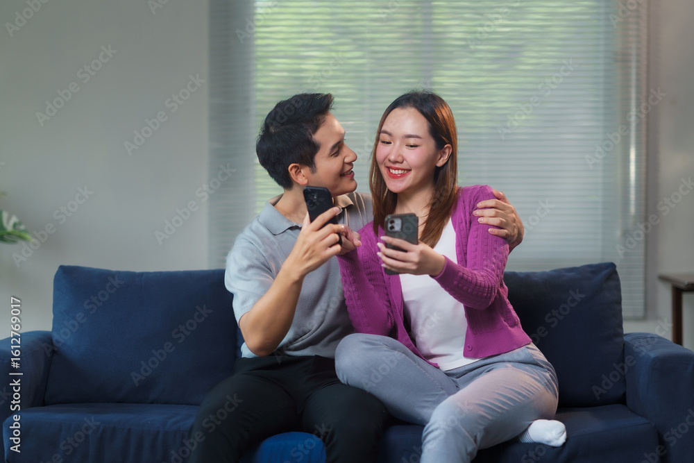 Young Asian couple sitting together on a sofa in a cozy living room ...