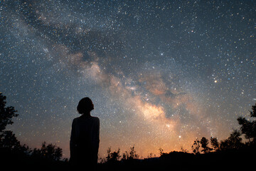 Wall Mural - silhouette of a young woman looking up at the milky way in a starry night sky, evoking a sense of wo