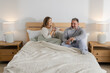 © Wavebreak Media - Couple wearing pajamas and holding ceramic mugs while sitting on bed at home with wooden headboard