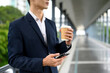 © Prathankarnpap - Businessman stands on an outdoor walkway with a paper coffee cup in hand and mobile phone