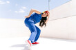 © VISTA by Westend61 - Woman doing hip hop dance pose outdoors in blue outfit with red hat