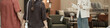 © DragonImages - Caucasian young adult woman standing and gesturing while talking to couple holding hands, engaging with customers in furniture store showroom with various seating options visible