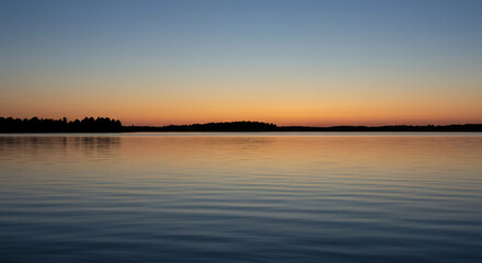Wall Mural - gentle ripples on a still lake at dusk, reflecting the soft hues of the twilight sky and distant sil