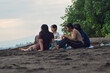© agratitudesign - Surrounded by coastal greenery, four teenage girls enjoy breakfast snacks on a mat while soaking up the relaxed seaside morning atmosphere.