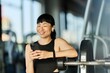 © bnenin - Smiling Woman at Gym Checking Smartphone During Break From Workout
