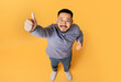 © Prostock-studio - Above Shot Of Cheerful Asian Man Showing Thumbs Up At Camera, Happy Excited Millennial Male Gesturing Sign Of Approval While Standing Over Yellow Studio Background, Top View, Copy Space