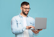 © Prostock-studio - happy adult caucasian guy with glasses prints on the computer works remotely isolated on blue background.