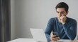 © Dhiditz - Thoughtful man using smartphone at home office with laptop on desk