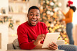 © Prostock-studio - Great offer, cashback and huge discount in new year. Young surprised and expresses success african american guy using tablet, lady in Santa hat decorates Xmas tree in living room with glowing garlands