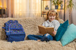 © Andrii Iemelianenko - Young teenager girl taking a fairy tale book from backpack at home, flipping reading pages with interest. Blonde child kid on sofa pauses to admire illustrations, grinning at each charming scene.