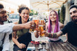 © TrueShot | Westend61 - Happy friends clinking beer glasses outdoors at a bar