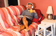 © jcalvera - Relaxed senior man reading a book, drinking tea and listening to music on sofa