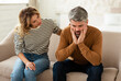 © Prostock-studio - Middle Aged Wife Comforting And Supporting Depressed Husband Sitting On Couch At Home. Couple Struggling And Suffering Having Problems. Male Depression And Midlife Crisis Concept
