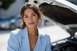 © Iryna - Young hispanic female in blue blazer smiling near open car hood in sunlight