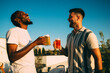 © djile - Two friends laughing and toasting with beer on rooftop at sunset