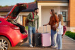 © Home-stock - Family putting baggage suitcases in their car, relocating to new home or preparing for vacation, standing neat automobile outside big house