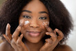 © Prostock-studio - Closeup portrait of attractive millennial black lady applying facial cream under her eyes. Pretty African American woman taking care of skin, putting on nourishing lotion. Beauty and natural cosmetics