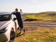 © mark_gusev - Male tourist is standing next to small rented car parked of road with amazing nature scenery in the background. Warm summer day with cloudy sky. Travel and tourism industry. Trip to nature.