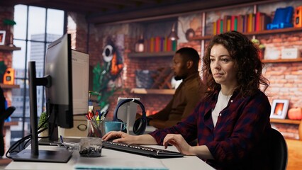 Smiling woman using programming languages on PC in IT startup office to build applications. Upbeat programmer using computer in software development agency to code, camera B