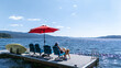 © Mat Hayward - Woman sitting on a dock overlooking a Lake. She is sitting on a blue chair under a red umbrella on a sunny day while on vacation relaxing.