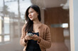 © Charlie's - Young Asian Woman Using Smartphone for Business Communication Outdoors in Urban City.