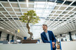 © BusinessClass by W61 - Smiling mature businessman standing by bonsai tree in industry