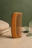 A close-up of a wooden comb resting on a neutral surface with a soft, blurred background