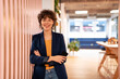 © BusinessClass by W61 - Happy young businesswoman standing with arms crossed near striped wall in office