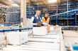© BusinessClass by W61 - Manager discussing over cardboard boxes with colleague by conveyor belt in warehouse