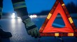 © Flash memory - A man places a red reflective warning triangle on the road at night. Roadside assistance and accident safety concept.