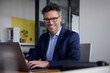 © BusinessClass by W61 - Happy businessman sitting with laptop at desk in office