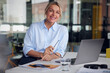 © BusinessClass by W61 - Smiling businesswoman holding eyeglasses and laptop at desk in office