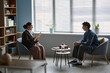 © Seventyfour - Female counselor holding clipboard talking with teenage boy sitting across in counseling session, both engaged in conversation in modern office setting