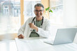 © BusinessClass by W61 - Smiling doctor sitting at desk with laptop in clinic