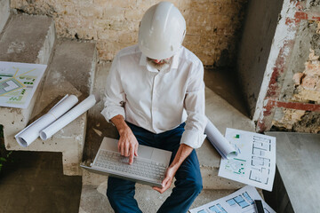 Architect using laptop with blueprints on staircase at site