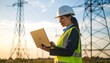 © somad - Female electrical engineer working on a laptop near power transmission towers