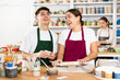 © JackF - Cheerful young man and woman in aprons modeling handmade mugs of row clay material in pottery workroom