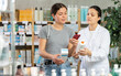 © JackF - Young girl choosing cream or skin care product in big pharmacy and scan QR code on label, young asian woman pharmacist consulting and offering variety of goods to customer