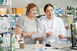 © JackF - Female pharmacist in a medical gown advises a mature woman near the cash register in a pharmacy. Pharmacist gives recommendations on the use of pills and selects vitamins according to a medical