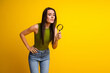 © deagreez - Woman in green top with magnifying glass poses thoughtfully against yellow background symbolizing curiosity and focus
