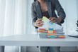 © Kritdanai - Organized Work: A professional meticulously organizes a stack of documents on a clean desk, the scene highlighted by soft natural light from a nearby window.