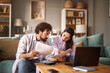 © Stockphotodirectors - Two individuals are focused on discussing their financial problems at home. They are surrounded by documents and a laptop, indicating a serious conversation.