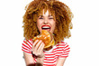 © VICHIZH - Smiling young woman with curly hair enjoying a hamburger, wearing a striped shirt, capturing joy and indulgence in a bright, cheerful setting