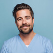 © Niks Ads - male doctor in light blue medical uniform smiling on blue background