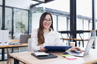 © SOMKID - Asian business woman working with laptop and analyzing financial charts at a desk.