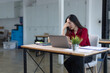© SOMKID - feeling stressed asian businesswoman working on laptop sitting at desk in modern office space for work online.